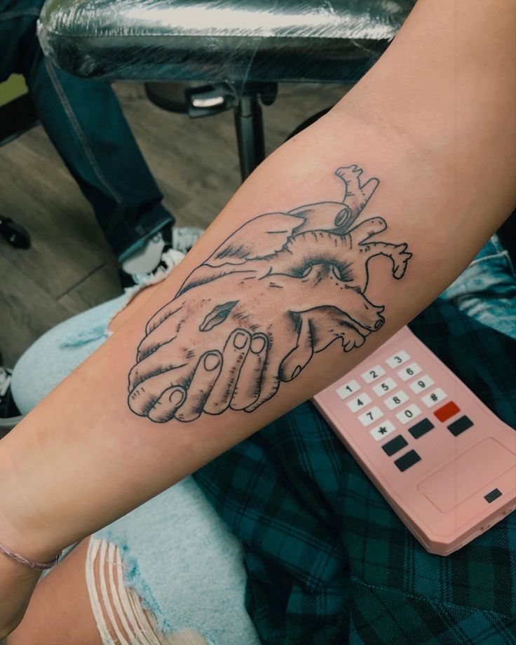 a person with a tattoo on their arm holding the hand of another person's heart