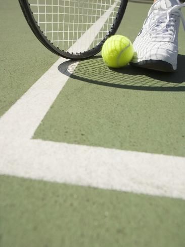 a tennis ball and racket are on the court, with someone's feet in the air