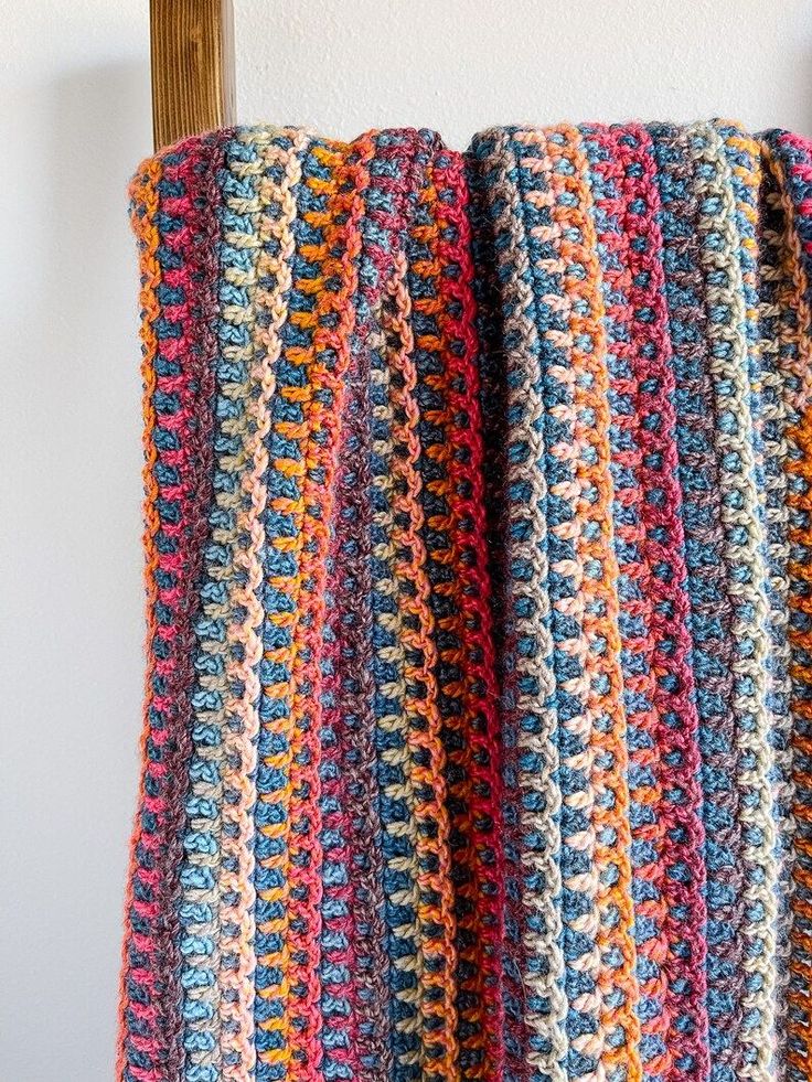 a multicolored crocheted blanket hanging up on a wooden chair next to a white wall