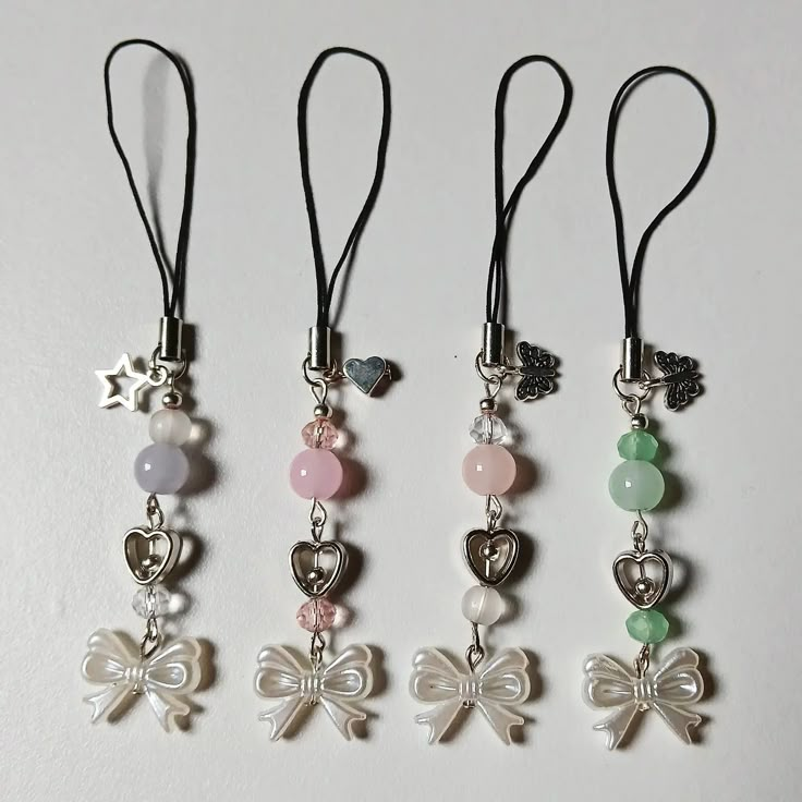 four necklaces with charms attached to them on a white surface and one has a bow