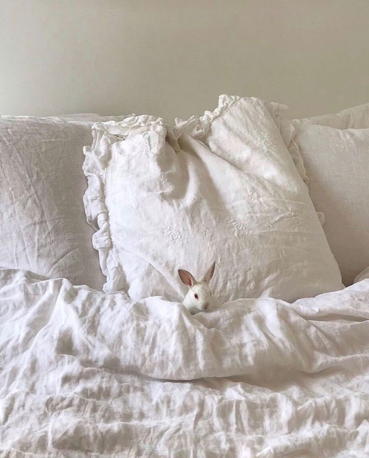 an unmade bed with white linens and a bunny head sticking out of the pillow