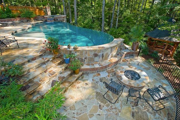 an outdoor swimming pool surrounded by stone steps and patio furniture with trees in the background