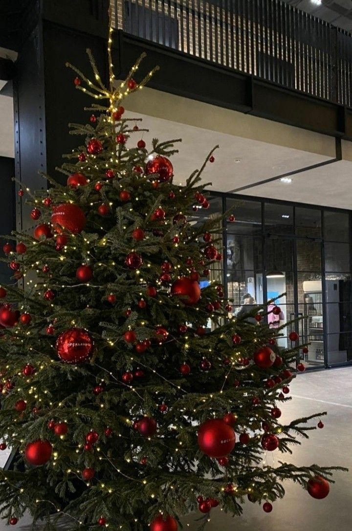 a large christmas tree with red ornaments in an office building's lobby, decorated for the holiday season