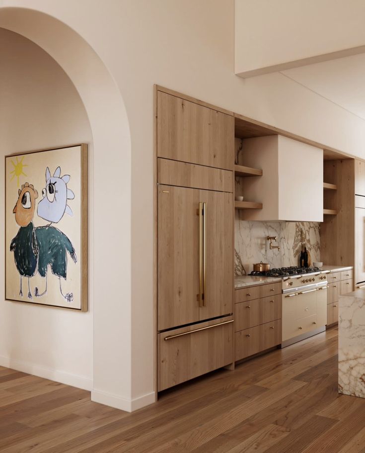 a kitchen with wooden floors and white walls, an art piece hanging on the wall