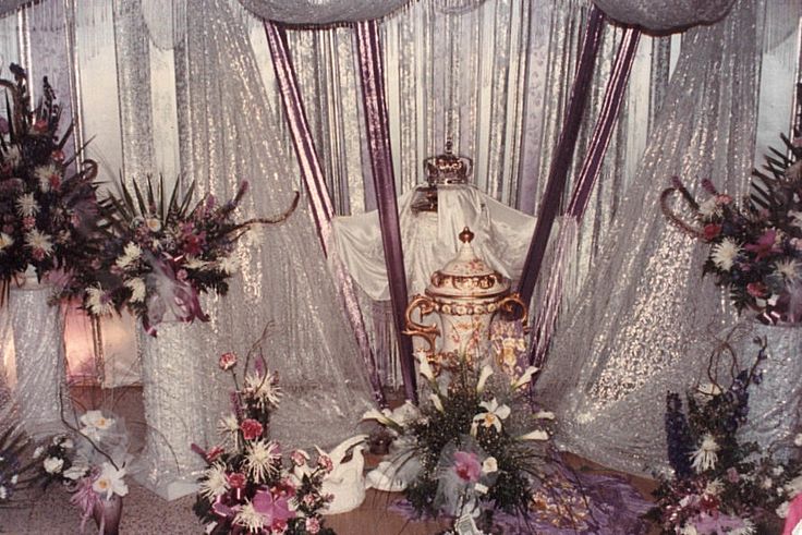 an elaborately decorated room with flowers, candles and vases on the floor in front of sheer curtains