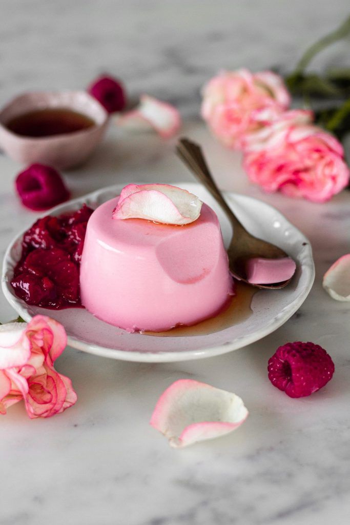 there is a dessert on the plate with pink flowers around it and two spoons