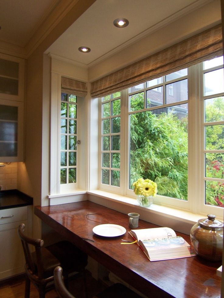 a table with a book and vase on it in front of a window that has trees outside