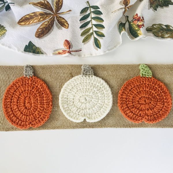 three crocheted pumpkins sitting on top of a burlocked placemat