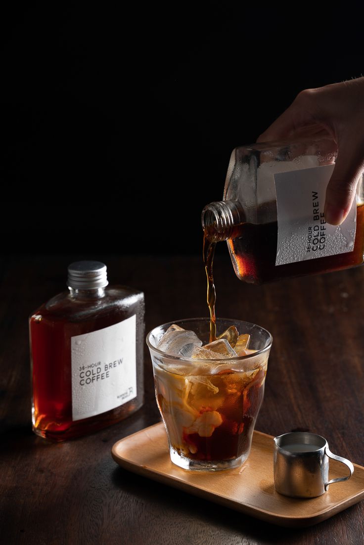 a person pouring syrup into a glass on top of a wooden table