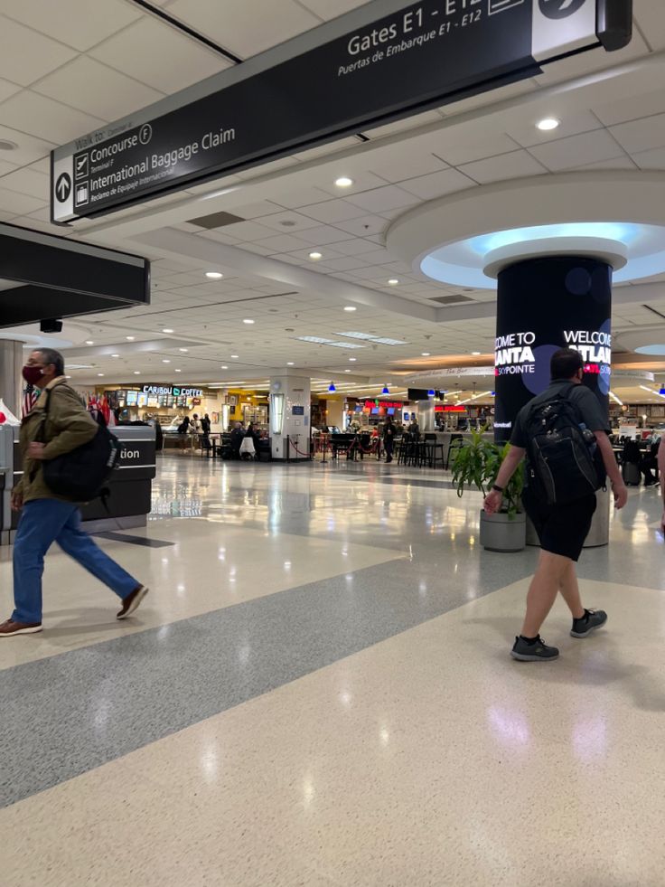 two people walking through an airport with luggage on their back and one person carrying a backpack