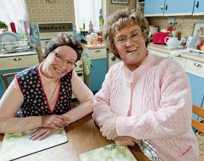 two women sitting at a table in a kitchen with an open book on the table