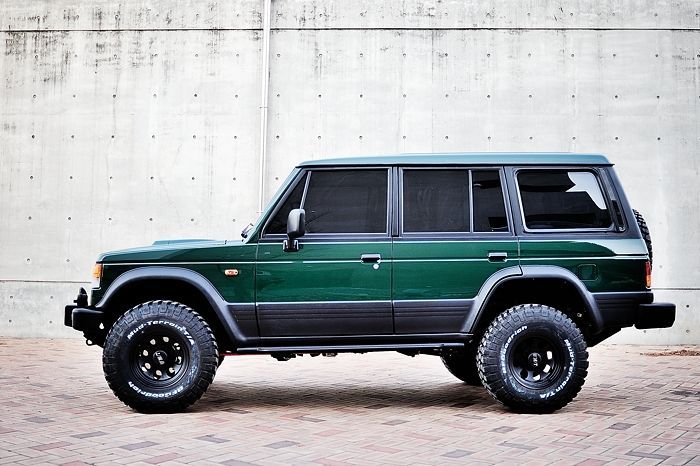 a green and black jeep parked in front of a concrete wall on a brick floor