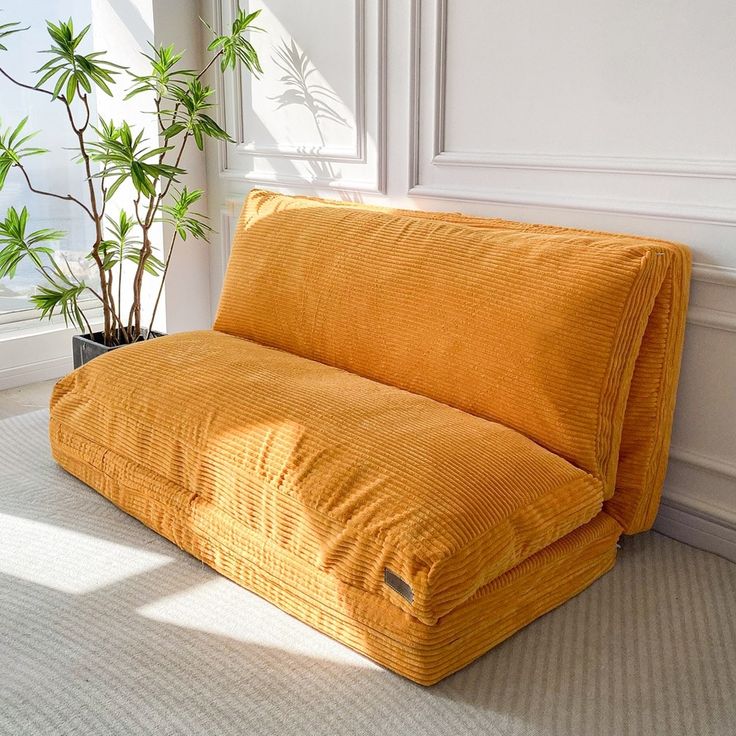 an orange couch sitting in front of a window next to a potted plant on the floor