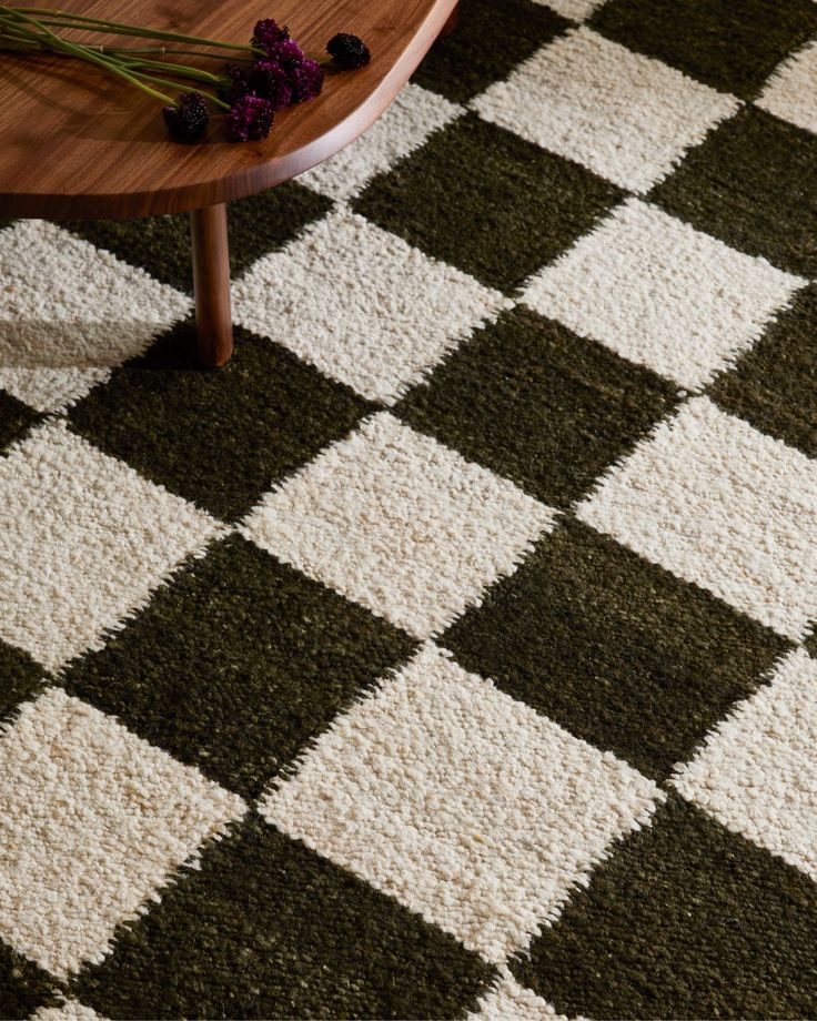 a coffee table sitting on top of a checkered rug next to a vase with flowers