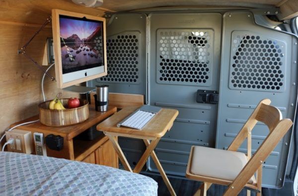 the interior of an rv with a bed, desk and television on it's wall