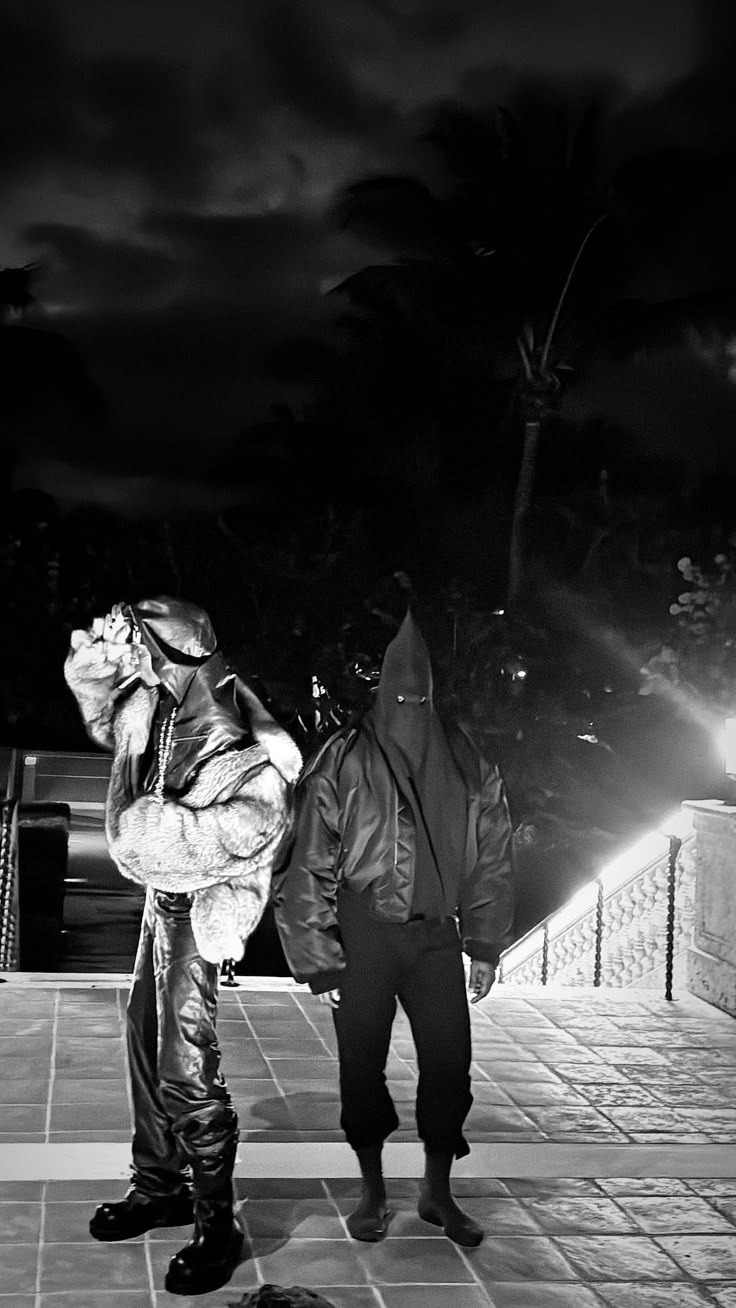 black and white photograph of two people dressed in costumes standing on a sidewalk at night