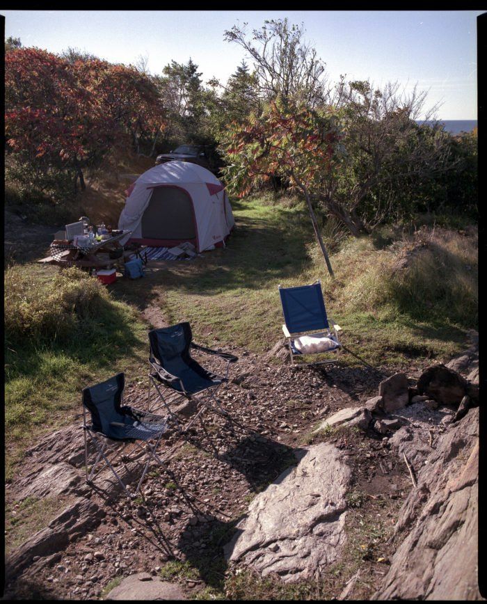 there are two chairs and a tent on the side of a hill with trees in the background