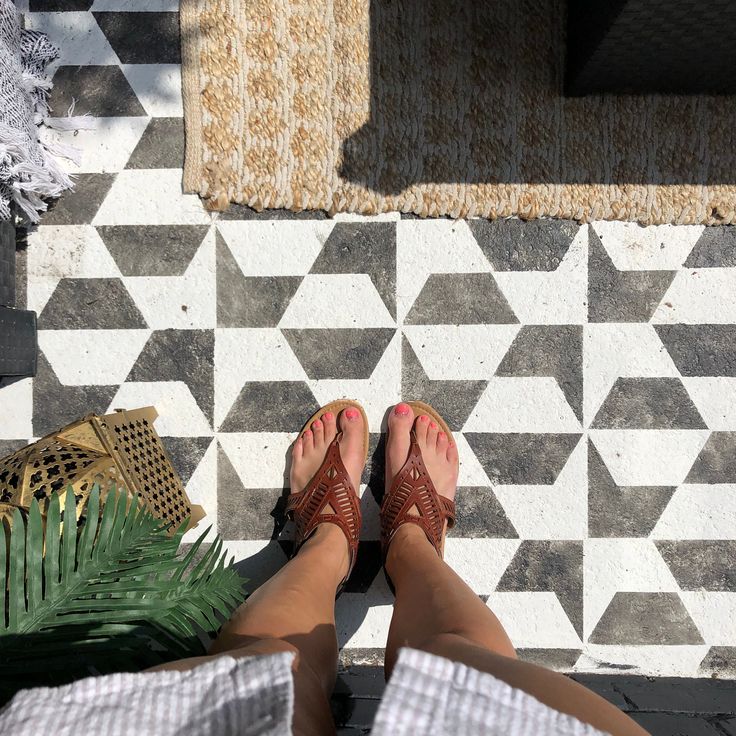 a person's feet with sandals on sitting next to a potted plant and rug