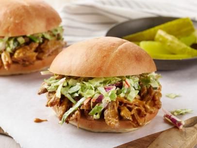 two pulled pork sandwiches with lettuce, carrots and ketchup on a white plate