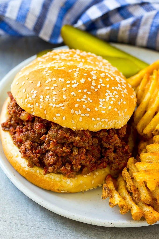 a sloppy joe sandwich and french fries on a plate with pickle wedges next to it