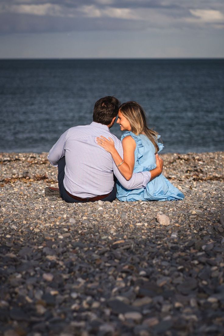 a man and woman are sitting on the beach looking at the ocean while holding each other