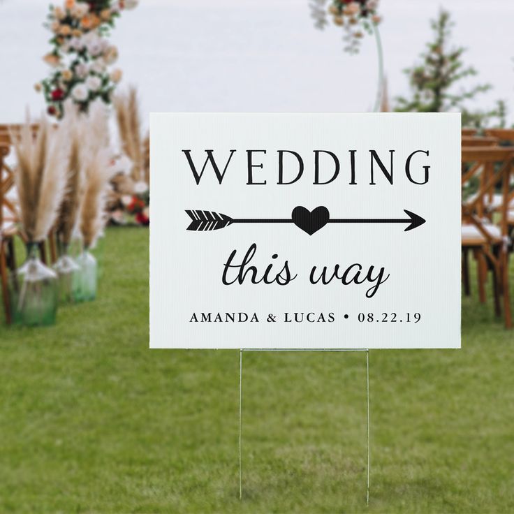 a sign that says wedding this way with an arrow and heart on it in the grass