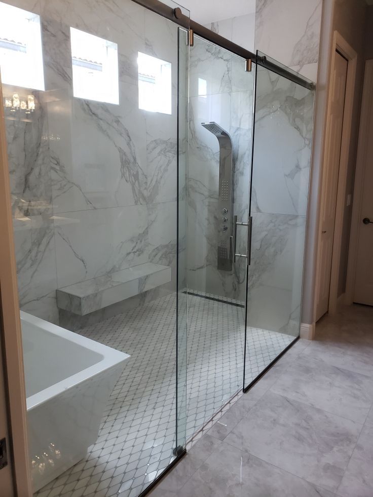 a bathroom with marble walls and flooring, glass shower doors and a white bathtub