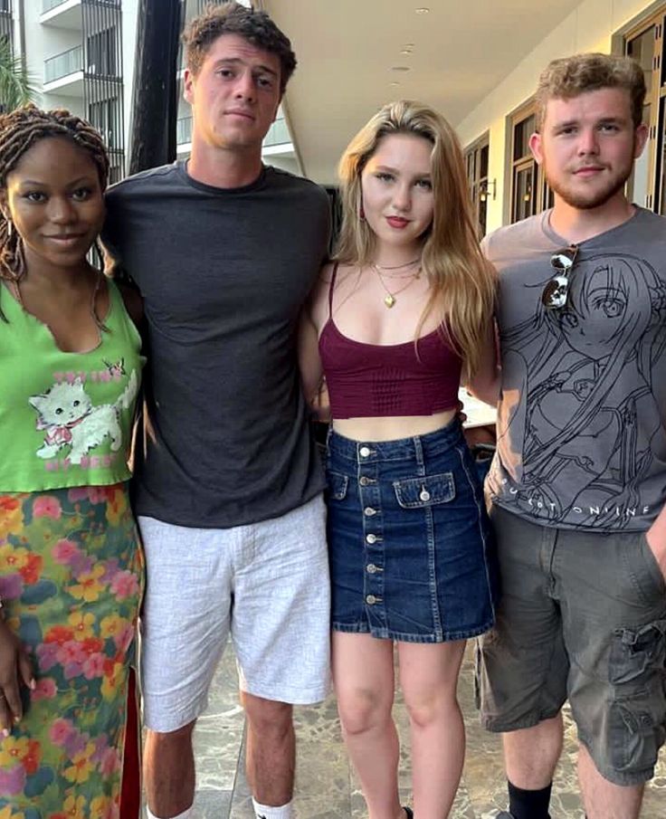 four people are posing for a photo in front of a building and one person is wearing shorts