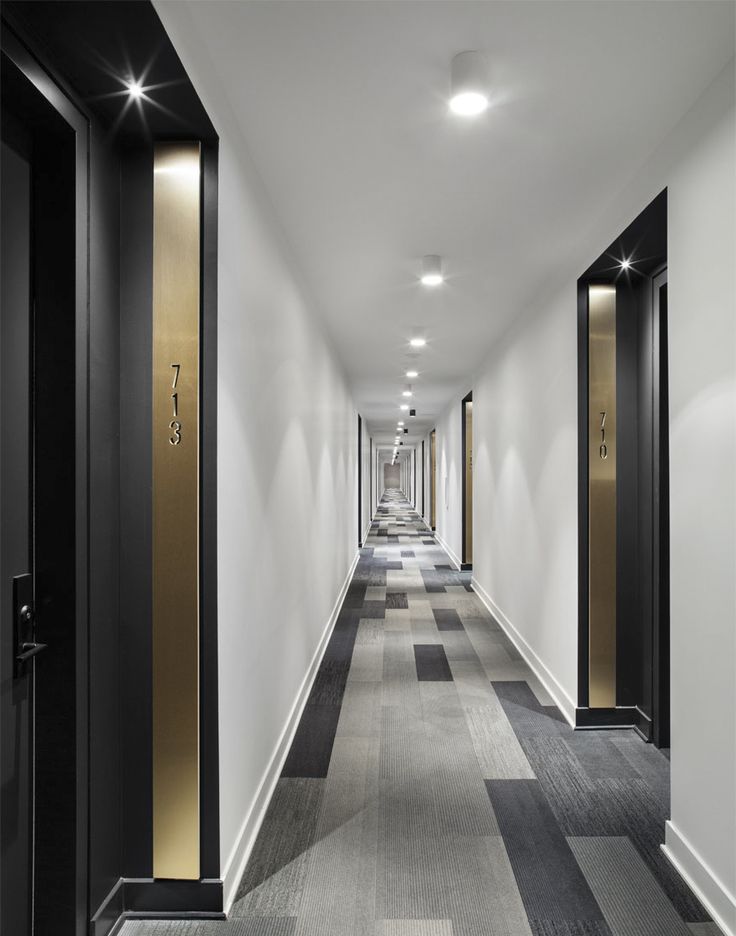 a long hallway with black and gold doors leading to the rooms on either side is an elevator