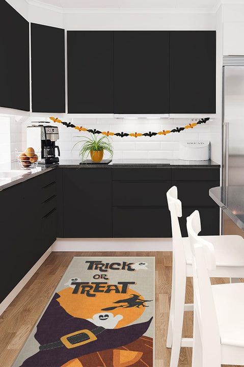 a kitchen with black cabinets, white chairs and an area rug that says trick or treat