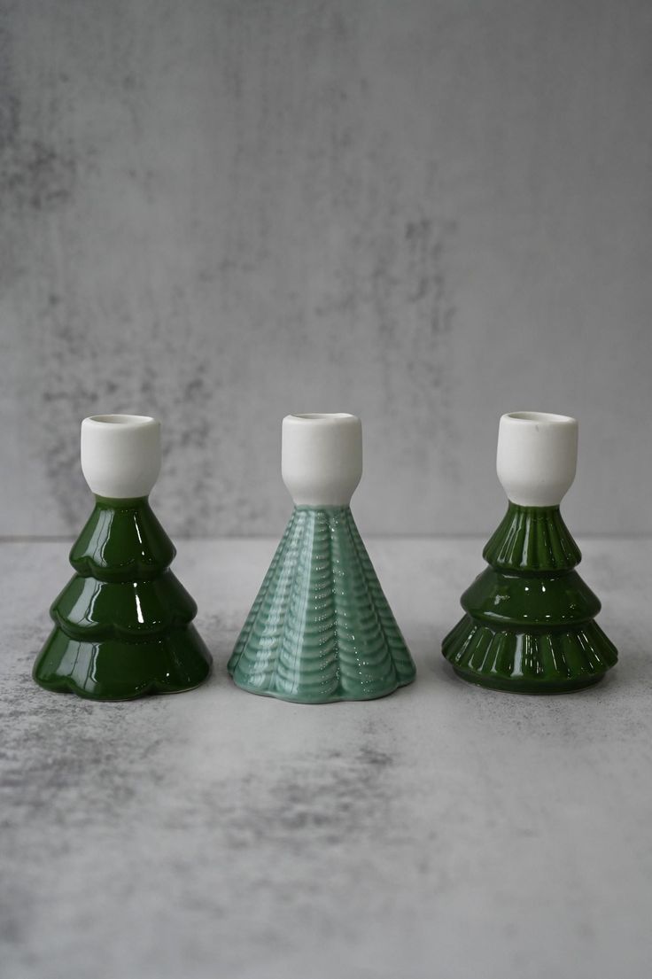 three small green and white vases sitting next to each other on a gray surface