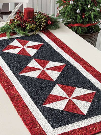 a red and black table runner on top of a dining room table with christmas trees in the background