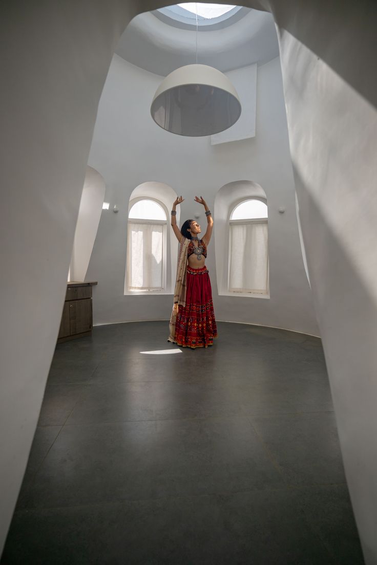 a woman in a red and gold dress standing in a white room with arches on the ceiling