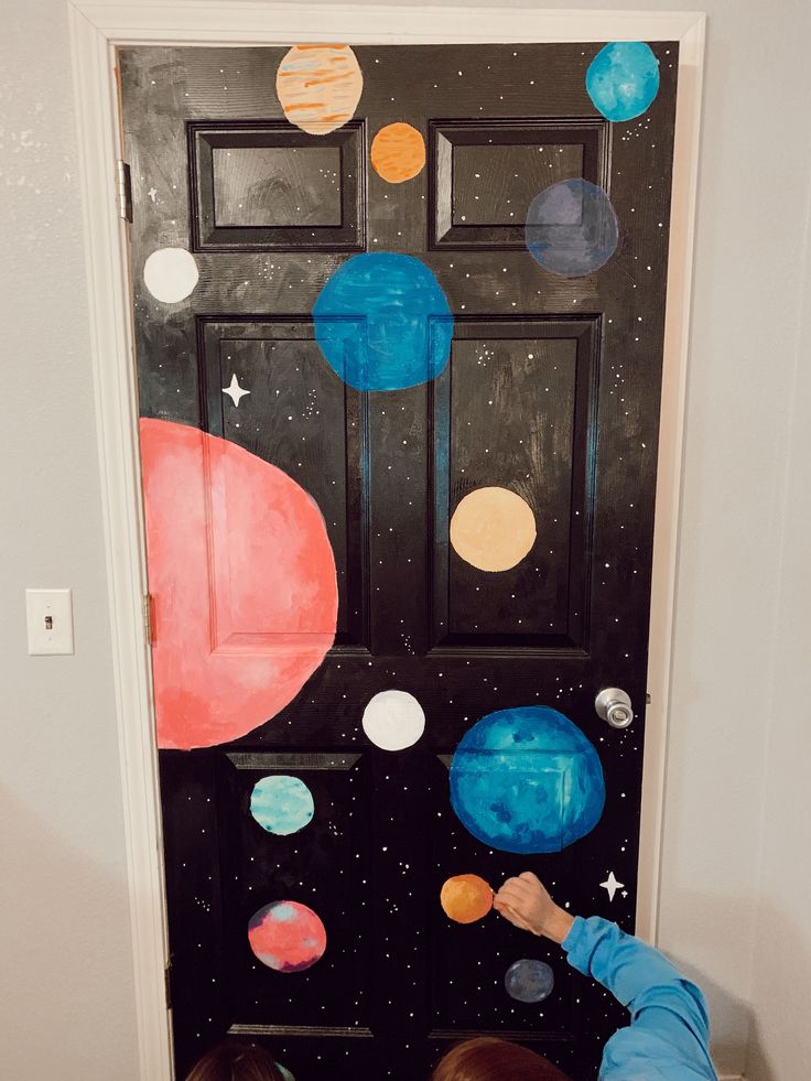 two children are playing in front of a door decorated with planets