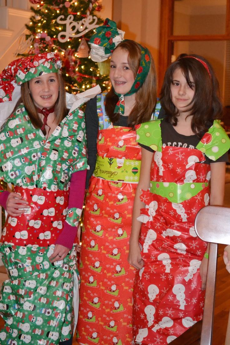 three girls in christmas pajamas standing next to a christmas tree with presents wrapped around them