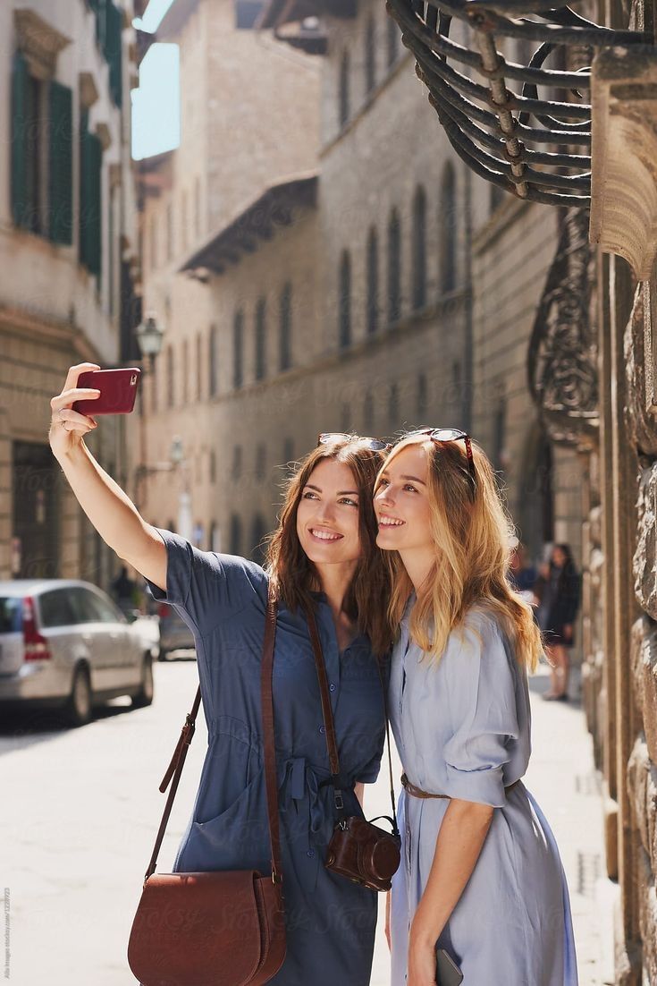 two women taking a selfie in an old european street with cars and buildings behind them