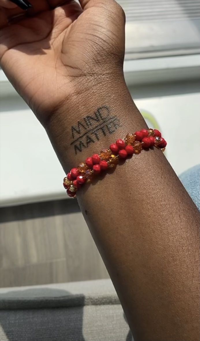 a person with a tattoo on their arm holding a cell phone and wearing a red beaded bracelet