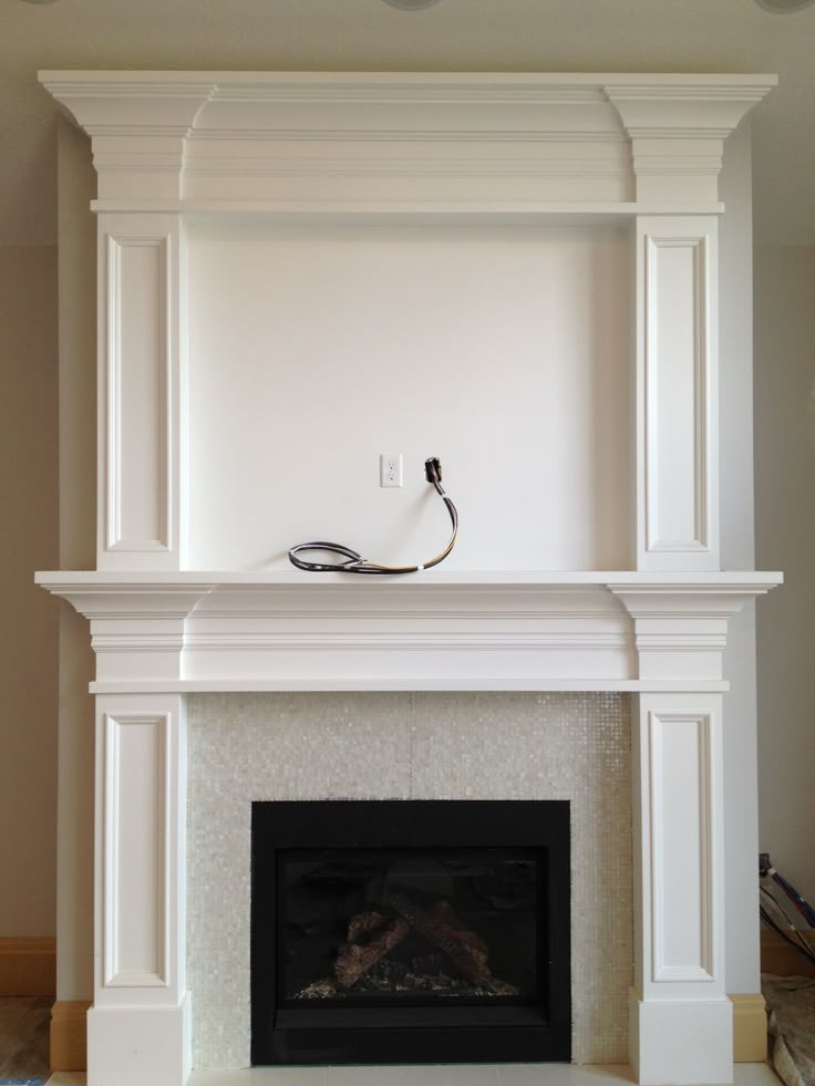 a fireplace with a white mantle and an electrical outlet on the mantel above it