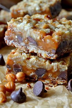 three pieces of candy bar sitting on top of parchment paper next to chocolate chips and nuts