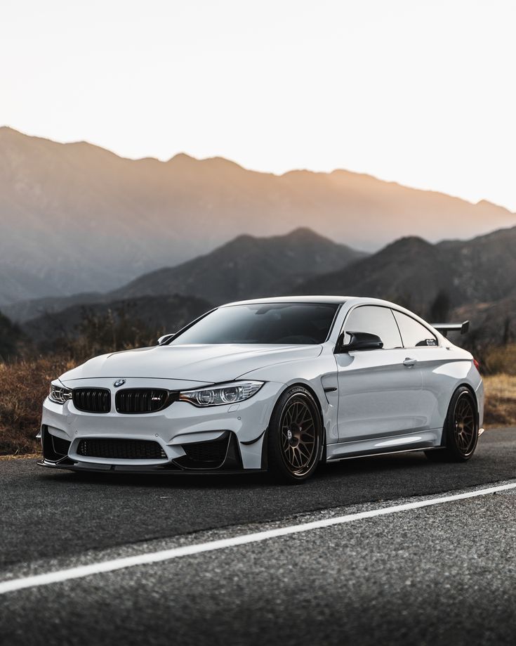 a white car parked on the side of a road in front of mountains and trees