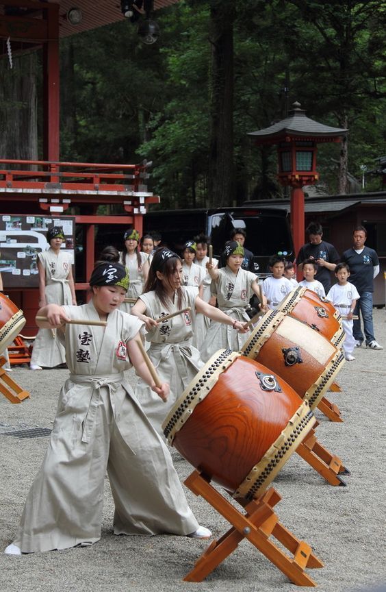 a group of women in traditional japanese garb dancing with large wooden drums and sticks