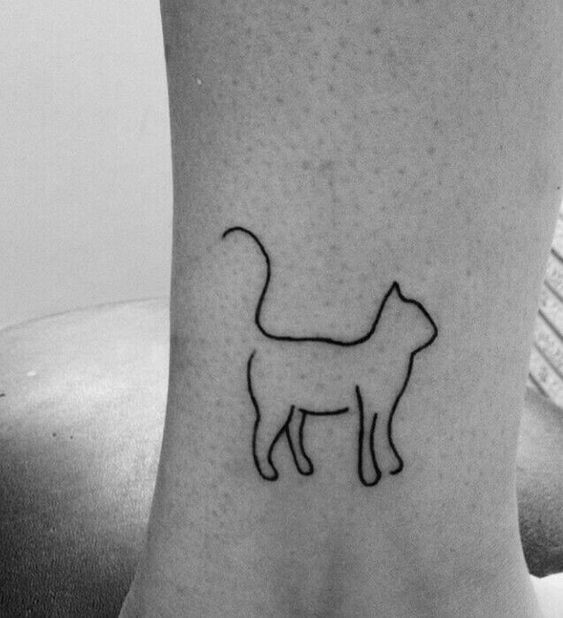 a black and white photo of a cat tattoo on the ankle, which has a small outline of a cat