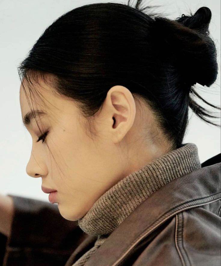 a woman wearing a brown leather jacket looking down at her cell phone while she's in profile