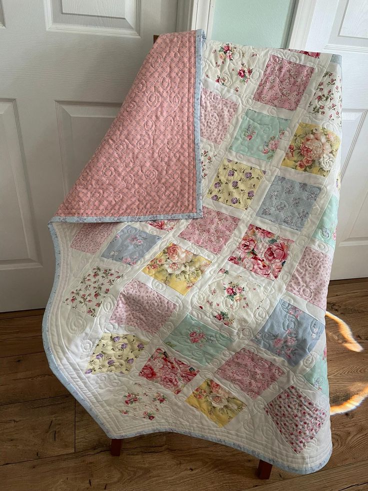 a pink and blue quilted blanket sitting on top of a wooden floor next to a white door