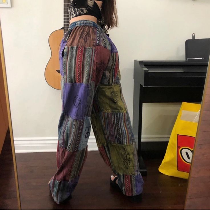 a woman standing in front of a mirror with her back to the camera, wearing colorful pants