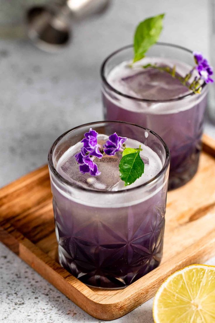 two glasses filled with lavender lemonade and garnished with purple flowers on a wooden tray