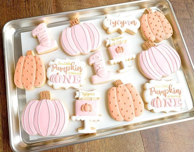 some decorated cookies are in a tray on a wooden table and there is a sign that says pumpkin love