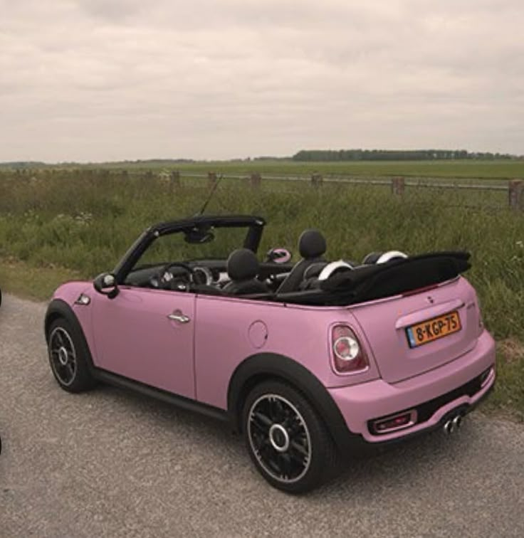 a pink convertible car parked on the side of a road next to a black motorcycle