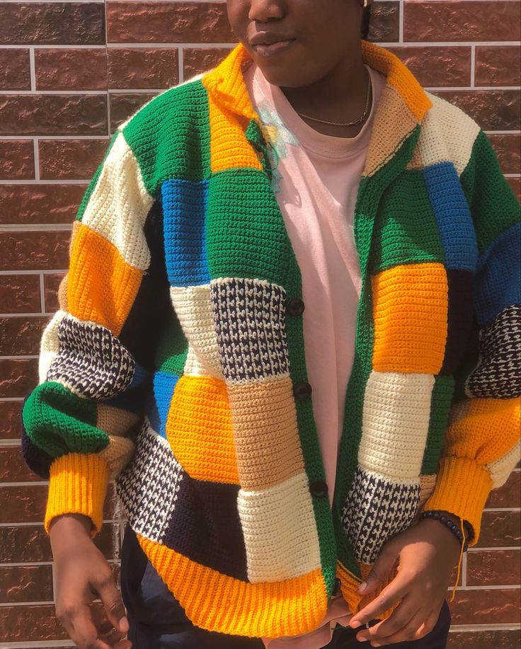 a woman standing in front of a brick wall wearing a multicolored knitted jacket