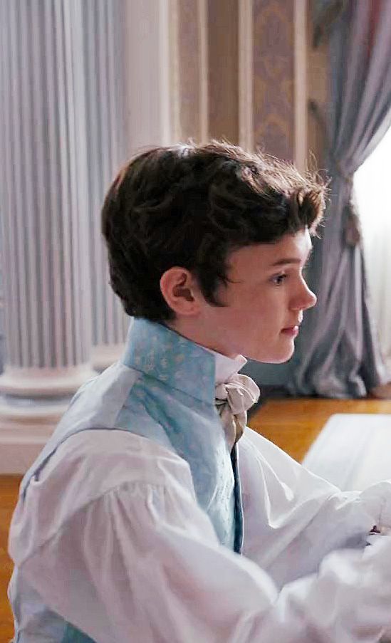 a young man sitting at a desk in front of a laptop computer wearing a white shirt and blue tie